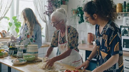 Elderly woman kneading dough as young grandson watching and granddaughter stirring pot during family cooking time in kitchen - Powered by Adobe