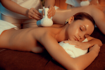 Hot herbal ball spa massage body treatment, masseur gently compresses herb bag on couple customer...