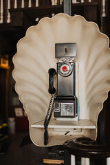 Vintage coin-operated rotary payphone with scallop-shaped booth backing and black handset,...