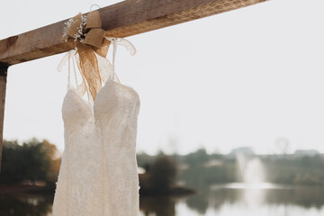 Ivory lace bridal gown with beaded floral embroidery hanging on rustic wooden arch decorated with...