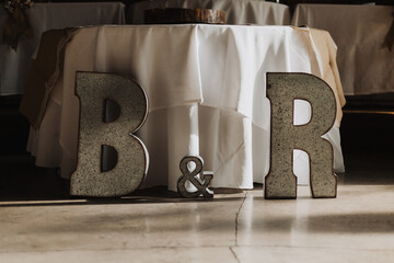 Rustic metal letters B and R with ampersand in front of round white table with burlap runner in warm indoor lighting for personalized wedding reception decor