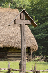 Traditional wooden roadside cross stands prominently in the foreground of this rural scene,...