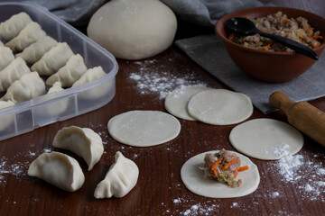 Stuffing pork gyoza with vegetable filling on raw dough rounds folding dumplings on floured wooden board home cooking traditional Japanese meal step by step process in kitchen close up
