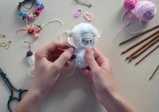 Handmade soft toy process with hands knitting small plush animal using crochet hook wool yarn, creative hobby craft table scene close up step by step DIY project, Step 2 - to sew all details of toy