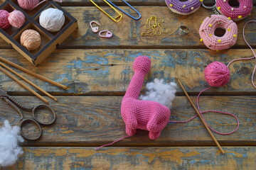 finished pink amigurumi dinosaur toy standing on table with wool yarn stuffing scissors crochet...