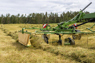 Making hay with the hay tedder. Farm Machine Tractor With Rotating Rake Attachments. Close Up Shot. Tractor with tedder shaking mowed grass.
