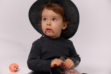 Toddler wearing witch costume holding halloween bucket with fake blood on face