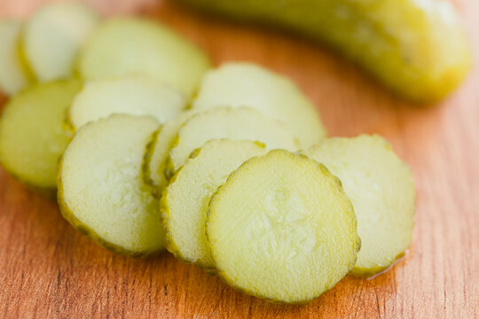 Slices of sour fermented pickled cucumber, pickle or gherkin on wooden board (Selective Focus, Focus through the middle of the first slice)