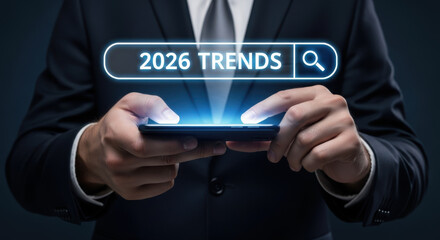 A businessman uses a smartphone to search for 2026 trends on a glowing digital interface