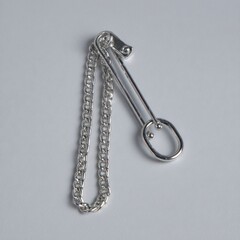 A silver metal chain with a unique clasp and oval, minimalist design on a gray backdrop