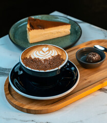 Mocha coffee with chocolate shavings and heart latte art served with truffle and Basque cheesecake on a wooden tray. 