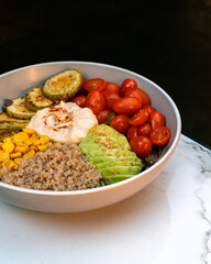 Healthy buddha bowl with hummus, quinoa, avocado, cherry tomatoes, grilled zucchini, corn and sesame. Colorful vegan meal in ceramic bowl. 