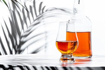 Single malt scotch whisky in a glencairn glass beside a bottle and decorative shadows on a table