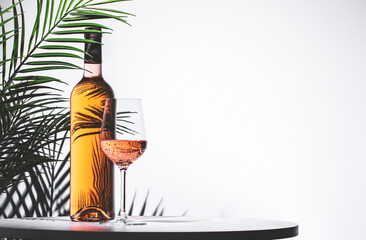 Rose pink wine served in an elegant glass beside a bottle against a light background with green...