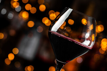 Close-up of a glass filled with red wine highlighted by soft bokeh lights in the background,...