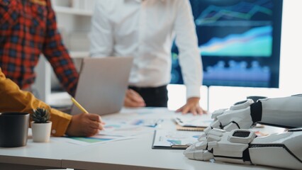 Professionals engage in a collaborative meeting with a humanoid robot, analyzing financial charts and data in a sleek, modern office setting.Noogenesis