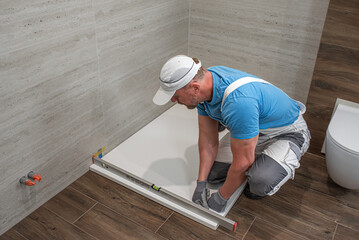 Installation of bathroom equipment. A worker measures the horizontality of a shower tray.