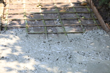Cement pouring on steel rebar grid during construction, cement pouring close-up with wet texture in daylight, cement pouring on reinforced foundation floor