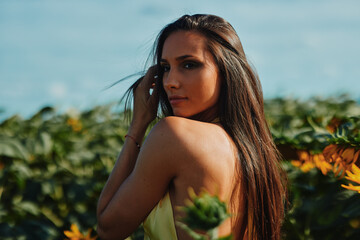 Beautiful young woman posing in sunflower field touching her hair