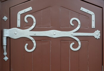 Decorative hinge with fine ornamentation on dark wooden door. Historic charm, handcrafted detail....