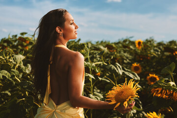 Beautiful woman wearing yellow dress holding sunflower in sunflower field