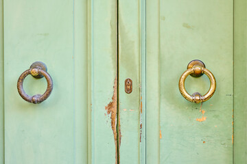 Two aged door knockers on green, weathered wooden door.