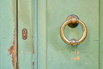 Old green wooden door with brass knocker and keyhole showing signs of wear and tear.