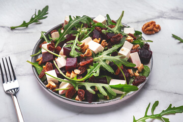 Gourmet beet salad with soft cheese, arugula, raisins and walnuts, marble table background, top view