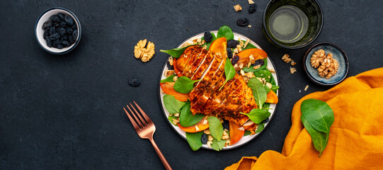 Autumn persimmon salad with grilled chicken breast, walnuts, raisin and spinach, black background,...