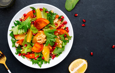 Delicious vegan salad with fresh persimmon, pomegranate seeds, walnuts, orange slices and lettuce