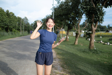 A woman is standing on a road, smiling and waving at the camera