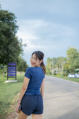 A woman in a blue shirt and shorts is walking down a road