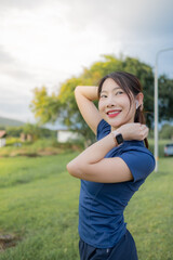 A woman in a blue shirt is stretching her arms in the grass