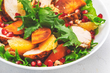 Yummy persimmon salad with grilled chicken, pomegranate, walnuts, oranges and lettuce, top view