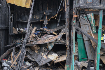Burned wooden structure with charred debris and broken framework after a severe fire.