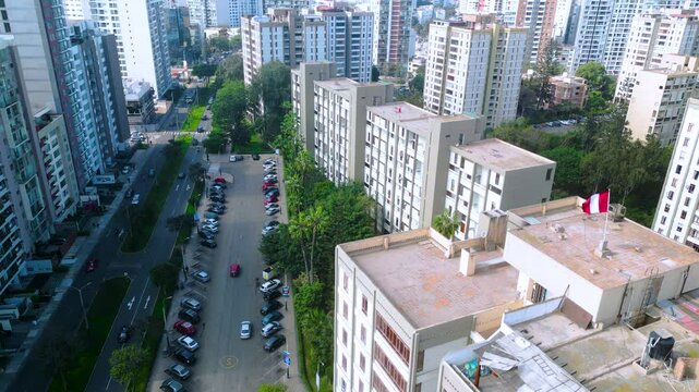 Bandera peruana ondeando en lo alto de un bloque residencial al lado de una avenida transitada en Lince, Lima.