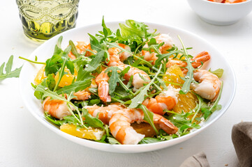Seafood salad with juicy shrimps and orange, arugula and sesame on white background, top view