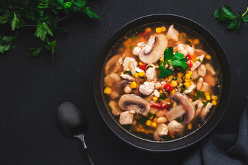 Mexican style chicken soup with mushrooms, corn, white beans, hot chili and cilantro. Black table background, top view