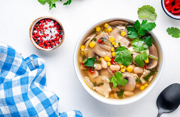 Mexican style chicken soup with mushrooms, corn, white beans, hot chili and cilantro. Black table background, top view