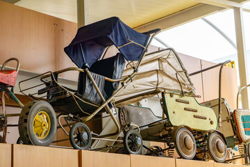 Old baby strollers from the communist era on a shelf. Retro models with metal frames and large...