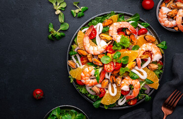Delicious seafood salad with shrimp, mussels, squid, oranges, lettuce and olive oil with lemon dressing, black background, top view