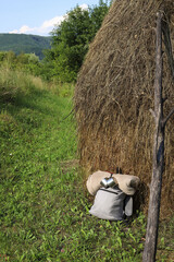 grey hiking backpack with folded blanket and tin mugs leaning against haystack in nature