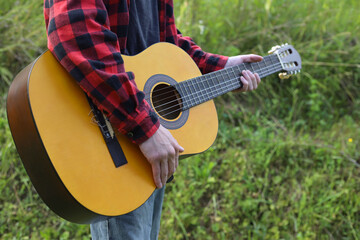 young guy in a red shirt with an acoustic guitar in nature