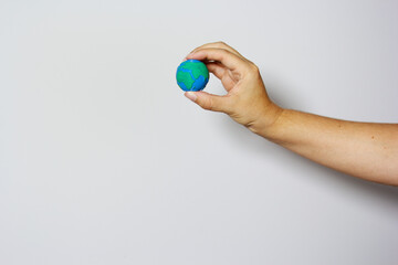 Single hand delicately grasping small Earth globe with fingers against neutral background, symbolizing environmental protection and care. Earth day concept. Environment day. 