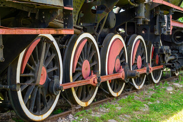 driving wheels of a vintage steam locomotive, painted black and red. Visible connecting rods and railway track.