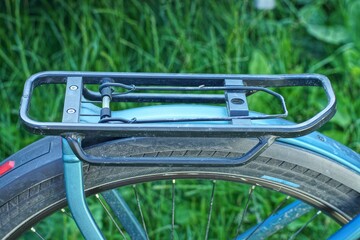 one empty black iron with spring  rear rack with part of blue frame wing and wheel with rubber tire from sport modern bicycle on green grass background in daytime outdoors