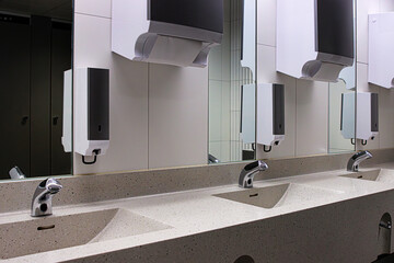 Interior of a modern public restroom with multiple sinks with chrome automatic faucets, mirrors,...