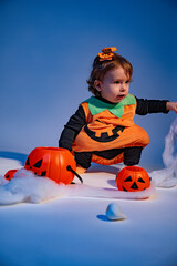 Baby girl wearing pumpkin costume playing with spider web and candy buckets for halloween