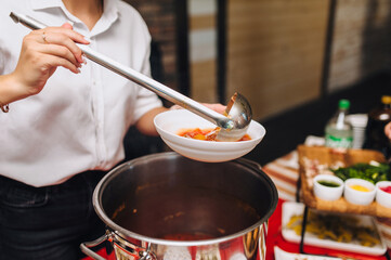 Photo of cook, waiter young woman pouring Ukrainian borscht from a large pot into a plate in a...