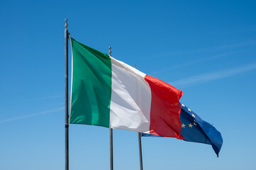 Green-white-red national italian flag and blue with stars flag of EU, waving on mast in sunny day in blue sky